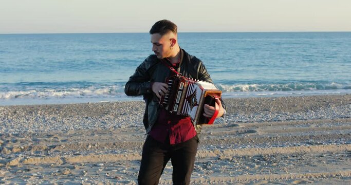 Ragazzo suona la tarantella calabrese con l'organetto in spiaggia vicino al mare