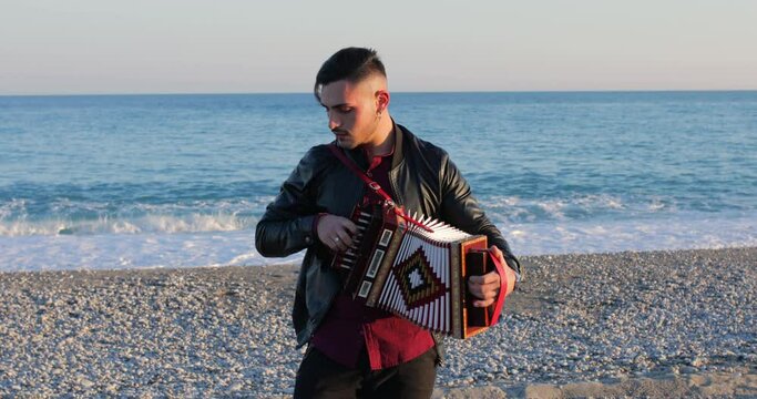 Ragazzo suona la tarantella calabrese con l'organetto musicale in riva al mare