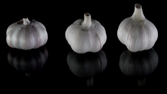 Close-up organic three heads of garlic shown from different angles, which are lying on a table, isolated on a dark background and spinning.