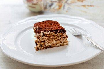 Close up on a portion of vegan tiramisu. Italian dessert on a white plate on wooden table