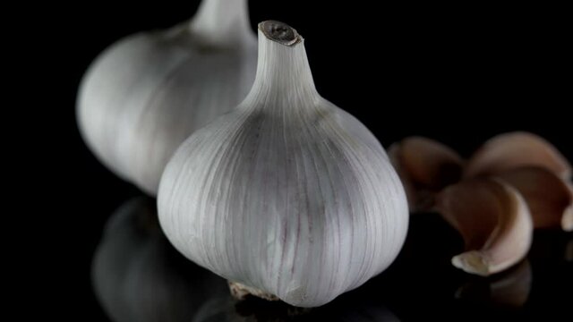 Close-up organic two garlic heads shown from different angles, which lie on a table, isolated on a dark background. Next to it are garlic cloves.