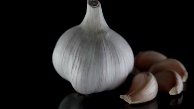 Close-up of an organic garlic head lying on a table, isolated against a dark background. Next to it are garlic cloves.