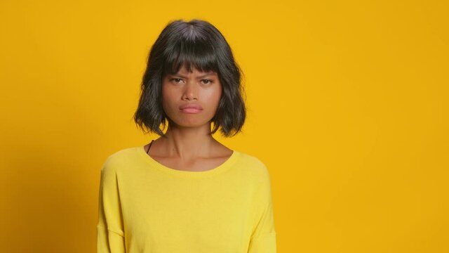 Unhappy serious dark skinned woman shakes head says no and disagrees with someone expresses disapproval denies something wears casual sweater poses against gold yellow background. Denial concept
