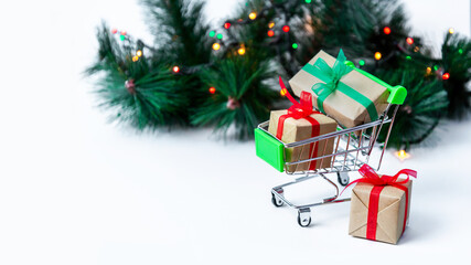 Banner. Small grocery cart with gift boxes on Christmas tree background with garland lights. Creative Christmas shopping online. Holiday sales and discounts for New year. Trading business. Copy space