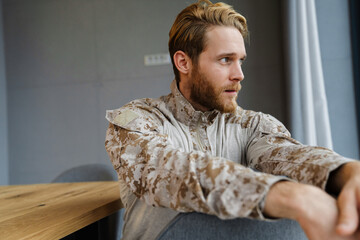 Masculine confident military man looking aside while sitting on chair