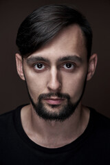 Obraz premium Portrait of handsome caucasian man with beard and stylish haircut in black clothes posing on brown background isolated in studio, fashion model looking at the camera