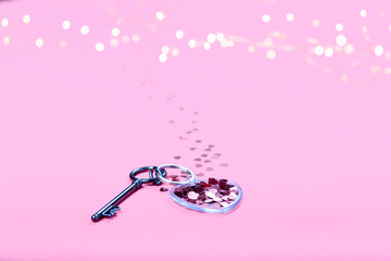 Key in shape of heart with confetti on keychain on pink background.