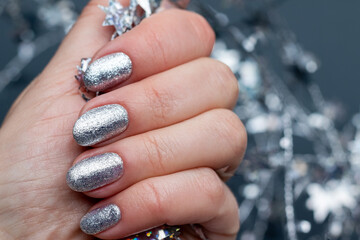 Female hand with beautiful holiday manicure - silver glittered nails with Christmas twisted wire with stars. Selective focus. Closeup view. Blurred gray background