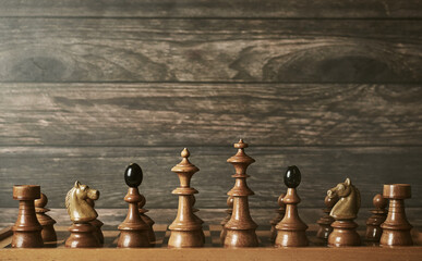 Vintage chess pieces arrangement on chessboard against wooden background