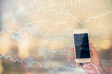 Double exposure of forex chart sketch hologram and woman holding and using a mobile device. Stock market concept.