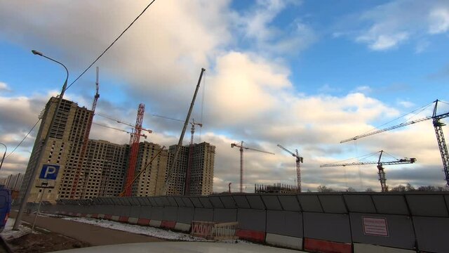 Timelapse work tower cranes when building a large office building against the background of fast running clouds in the blue sky.