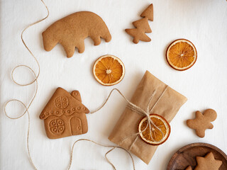 Gingerbread cookies of different shapes, gift wrapped in craft packaging, dried orange slices laid out on a white tablecloth in the morning light, top view