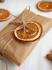 Gingerbread cookies of different shapes, gift wrapped in craft packaging, dried orange slices laid out on a white tablecloth in the morning light, top view