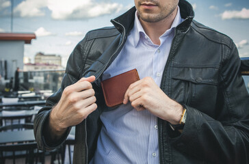 A man in a black leather jacket pulls out a wallet from an inside pocket - obrazy, fototapety, plakaty