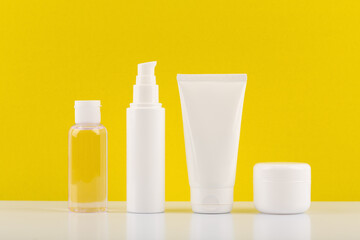 Face cream, cleaning foam, skin lotion and under eye cream on white table against bright yellow background