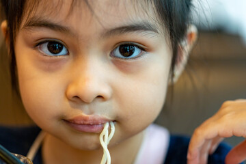Female asian child while eating noodles. Child eating ramen noodles smiling and enjoying the food. Child eating spaghetti