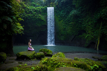 Young Caucasian woman sitting on the stone near the waterfall in Vajrasana or Diamond pose. Hands...