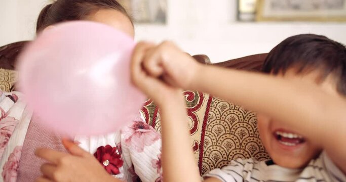 Slow-motion close of a boy and a girl playful fun enjoy naughty love care share inflating color balloons in living room on couch and fight hitting each other in between looking at camera pov