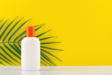 Sunscreen lotion in white jar with orange cap against yellow background with a palm with space for text