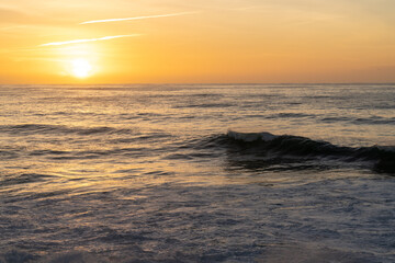 Obraz premium sunset over the ocean with colorful sky and large waves rolling in towards the coast