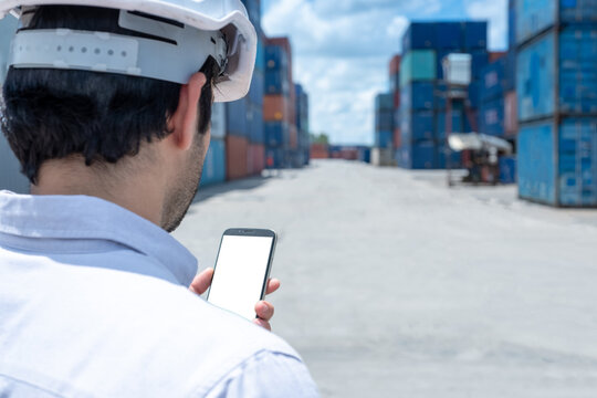Close up back view of engineer or business man using blank white screen mobile phone with containers shipyard background. Business Cargo Ship Import/Export Factory Logistic.