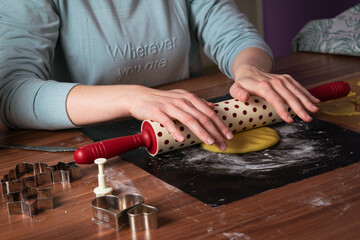 Young woman preparing christmas cookies on black baking sheet on table with dough roller 