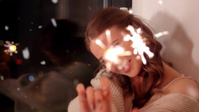 christmas, holiday and people concept - happy young woman with sparklers at home at night over snow