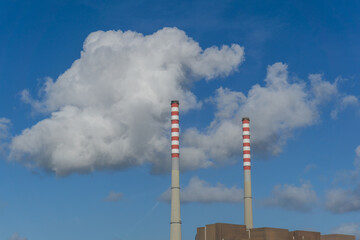 two tall smokestack chimneys of an industrial port factory under a blue sky and white clouds