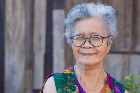 Senior woman wearing eyeglasses with short white hair smiling and looking at camera while standing in a garden. Concept of old people and healthcare