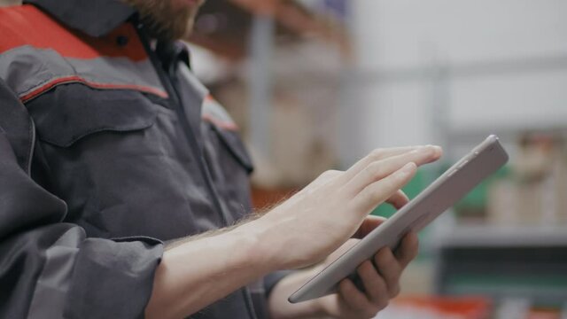 Midsection shot of unrecognizable male construction contractor in blue overall suit with laptop using tablet for inventory management working at warehouse