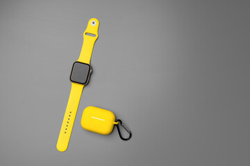 Yellow smartwatch and earphones in case on gray background