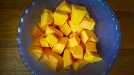 Square sliced pumpkin in a blue plastic bowl, on a wooden table. Theme on fruits and vegetables.