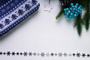 Christmas and new year concept with blue Christmas sweater, blue holly berries and silver star and silver christmas tree decoration. Whate backdrop. Copy space. Top view.