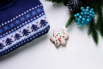 Christmas and new year concept with blue Christmas sweater, blue holly berries and star cookie. White backdrop. Copy space. Top view.