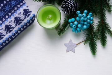 Christmas and new year concept with blue Christmas sweater, blue holly berries silver star and green candle. White backdrop. Copy space. Top view.