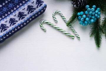 Christmas and new year concept with blue Christmas sweater, blue holly berries and green candy canes. White backdrop. Top view. Copy space.