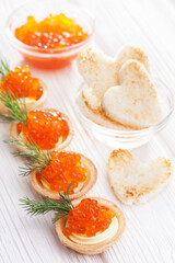 tartlets with butter and red caviar and dill on the white wooden table. Delicious snack
