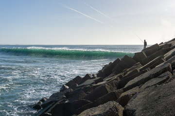 fisherman fishing on the rock jetty at Sao Torpes Beach in Sines
