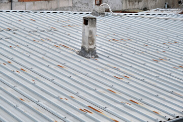 Roof of house made of metal panels. Corrosion exists on roof and old style chimney stack during overcast weather.