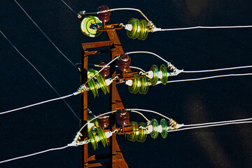 Glass electric insulators mounted on wires of old rusty powertower view from above