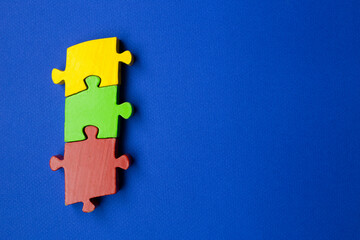 Obraz premium three puzzle pieces of different shapes and different colors are joined together to form a linear union. yellow, red and green pieces on a blue background. copy space