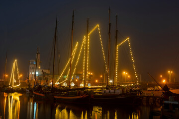 Decorated traditional sailing ships in the harbor from Harlingen in the Netherlands in christmastime at night