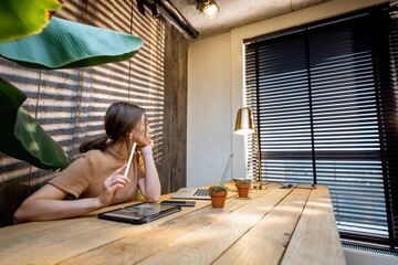 Creative woman in comfortable domestic suit working on digital tablet at the cozy and style home office