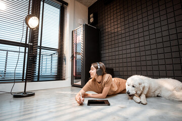 Young relaxed woman works on a digital tablet, lying with a dog on the floor at home music studio. Concept of working from home and home music studio
