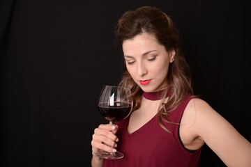 girl with red lips in a Marsala dress holding a glass of red wine in her hands on a black background