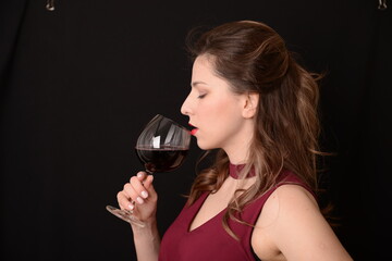 girl with red lips in a Marsala dress holding a glass of red wine in her hands on a black background