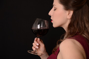 girl with red lips in a Marsala dress holding a glass of red wine in her hands on a black background