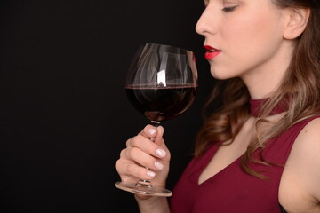girl with red lips in a Marsala dress holding a glass of red wine in her hands on a black background