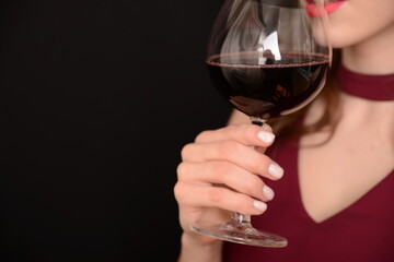 girl with red lips in a Marsala dress holding a glass of red wine in her hands on a black background