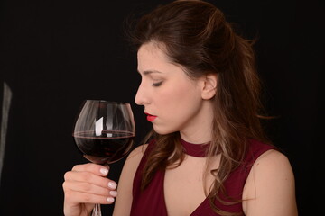 girl with red lips in a Marsala dress holding a glass of red wine in her hands on a black background